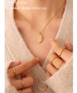 Close-up of golden oval queen pendant necklace and rope rings on beige knitwear