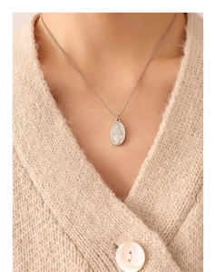 Detailed view of silver oval medallion necklace with relief on beige knit sweater