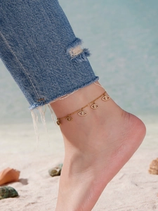 Bracelet de cheville doré avec pendentifs mauvais œil sur une plage de sable fin