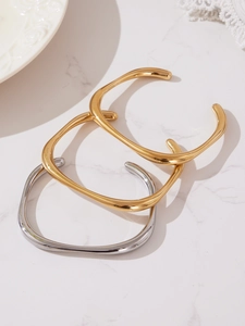 Détail de trois bracelets joncs ondulés polis en or et argent sur fond marbre