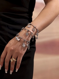 Detalle de pulseras plateadas con colgantes de trébol y árbol en la muñeca de la modelo