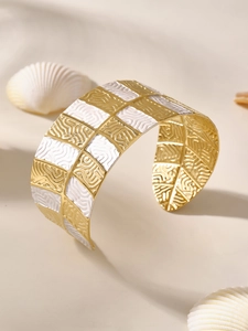 Dettaglio del bracciale rigido a scacchi oro e bianco con trama a onde su sfondo conchiglia