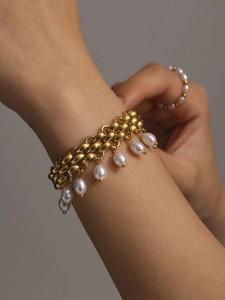 Détail d'un bracelet doré à gros maillons avec perles blanches et bague sur le modèle