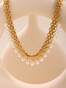 Vue détaillée d'un collier tressé doré avec perles blanches sur un support de bijoux