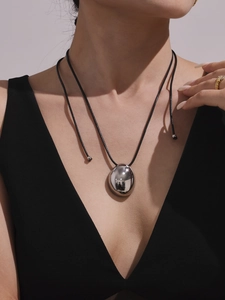 Polished gold teardrop pendant on black adjustable cord worn by a model in V-neck
