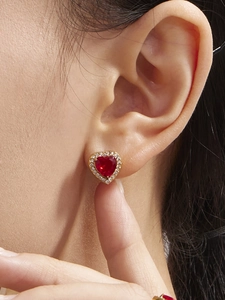 Close-up of heart-shaped red zircon earrings with halo diamond setting on gold base