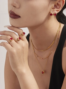 Detail of layered gold necklaces with ruby heart pendant and matching stone rings on model