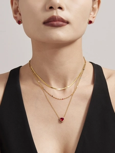 Close-up of three-layered golden necklace set with red heart zircon pendant and earrings