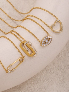 Macro shot of gold-plated necklaces with heart, eye, and pin charms on a stone stand