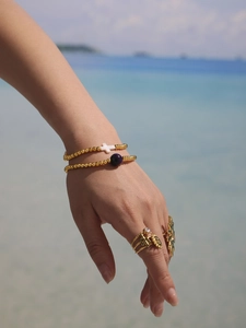 Close-up of 18k gold beads bracelets with cross pendant and agate on beach background