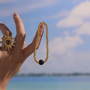 Golden bead bracelet with purple gemstone worn by model against a blue ocean background