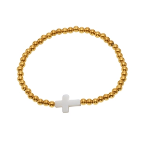 Elastic gold bead bracelet featuring a white shell cross charm on a plain background