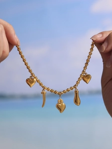 Detail of gold bamboo chain with heart and Italian horn charms over sea background