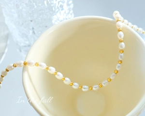 Baroque freshwater pearls and gold metal beads draped over an elegant cream ceramic cup