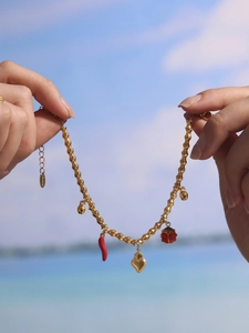 Detail of gold stainless steel bamboo chain bracelet with colorful charms against sea view