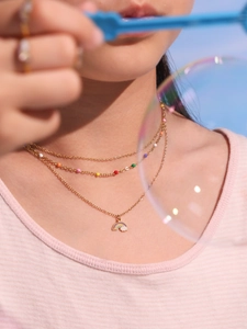 Close-up of triple-layered gold necklace with rainbow beads and cloud enamel pendant