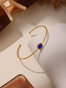 Detail des goldenen Armreifs mit blauem ovalem Edelstein und Strukturierter Metallring