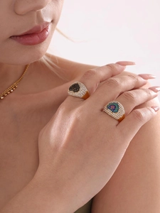 Détail de bagues en zircons plaquées or 18 carats avec motifs œil et cœur colorés