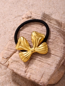 Macro detail of golden textured bow hair tie on a minimalist natural stone background