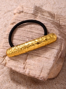 Macro detail of golden hammered metal cylinder decoration on black elastic hair tie