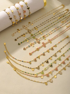 Détail de bracelets de cheville en acier doré avec breloques cœur colorées et zircons
