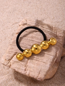 Close-up of golden metallic beads on a black elastic hair tie set on a natural stone
