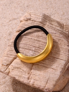 Detail of high-elastic black hair tie with curved gold metal decor on stone texture