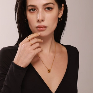 Gold necklace with bean pendant, hoop earrings and rings set on female model