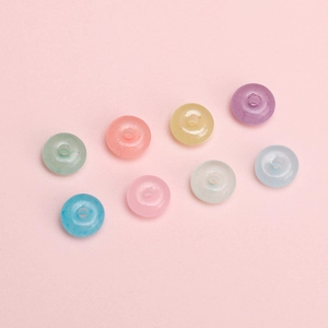 Colorful macaron glass beads in donut shape for DIY jewelry making on pink background