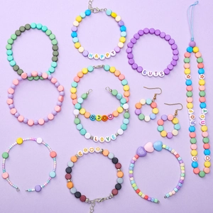 Plano cenital de pulseras de cuentas macaron coloridas y letras sobre un fondo violeta