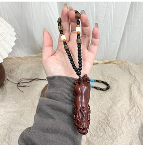 Detail of hand-carved wood Pixiu pendant with decorative beaded lanyard held in hand