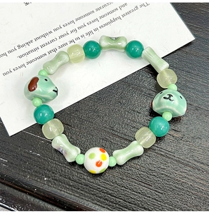 Detail of handmade ceramic bone and puppy charms on a green beaded bracelet
