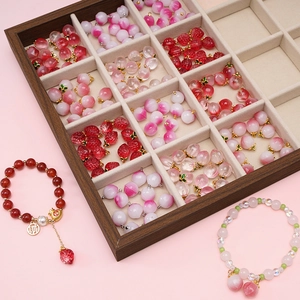 Ciondoli in vetro a pesca rosa e braccialetti di perline esposti su un vassoio di legno