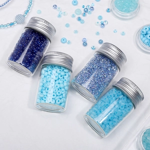 Detailed view of four small glass bottles filled with assorted 2mm blue seed beads for DIY jewelry
