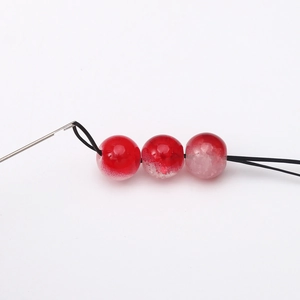 Bead threading tool kit featuring red gradient beads on black elastic cord and stainless steel needle