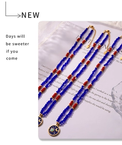 Dettaglio della collana di perle blu e rosse con ciondolo dorato a tema sole e luna
