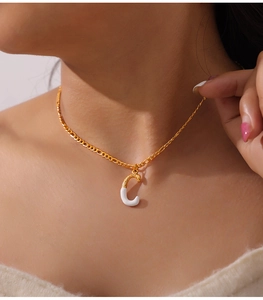 Macro view of golden Figaro chain with a white enamel letter C pendant on neck
