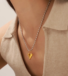 Vue rapprochée du pendentif cœur doré sur chaîne à billes argentée porté par un mannequin
