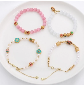 Dettaglio di perle floreali in smalto cinese e ciondoli dorati su braccialetti