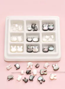 Detalle macro de cuentas de concha natural con forma de gato y conejo para joyería DIY