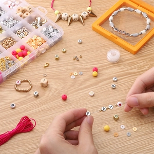 Manos enhebrando cuentas de arcilla de colores y letras doradas para joyería artesanal