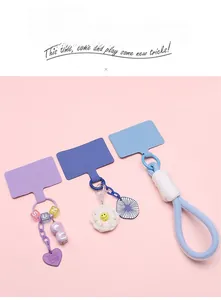 Three colorful phone lanyard patches with charms on a soft pink background
