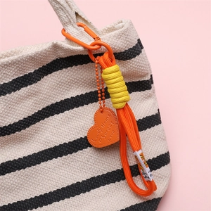 Colorful woven keychain with orange heart tag and carabiner on a striped bag