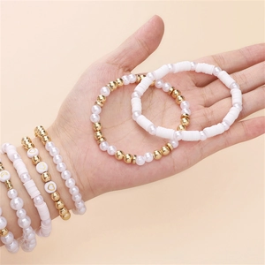 Détail de bracelets perlés avec perles blanches, dorées et disques d'argile sur le poignet