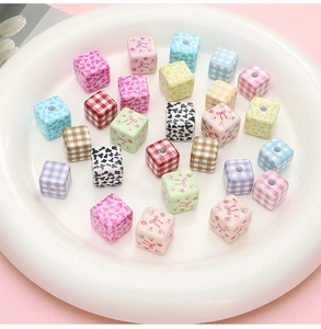 Macro detail of acrylic cube beads with diverse floral, bow, and plaid patterns