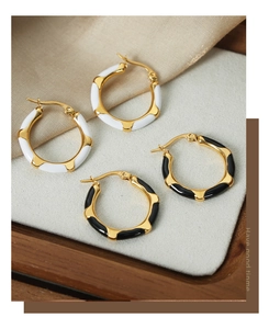 Detail showing gold-plated titanium earrings with black and white enamel drip glaze finish