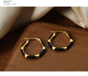 Detail view of geometric gold earrings with black enamel on a silk and wood display