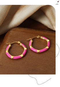 Detailed shot of gold plated earrings with pink enamel finish on wood background