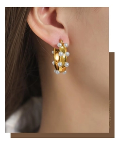 Close-up of elegant gold U-shaped earrings with hollow pearls on a model ear