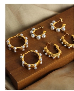 Detail of 18k gold plated U-shaped pearl earrings on a premium wooden display stand